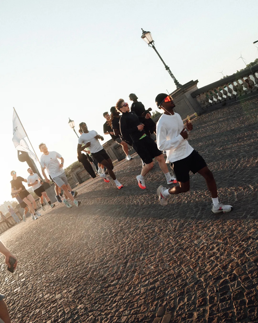Runners crossing a cobbled bridge in the evening light